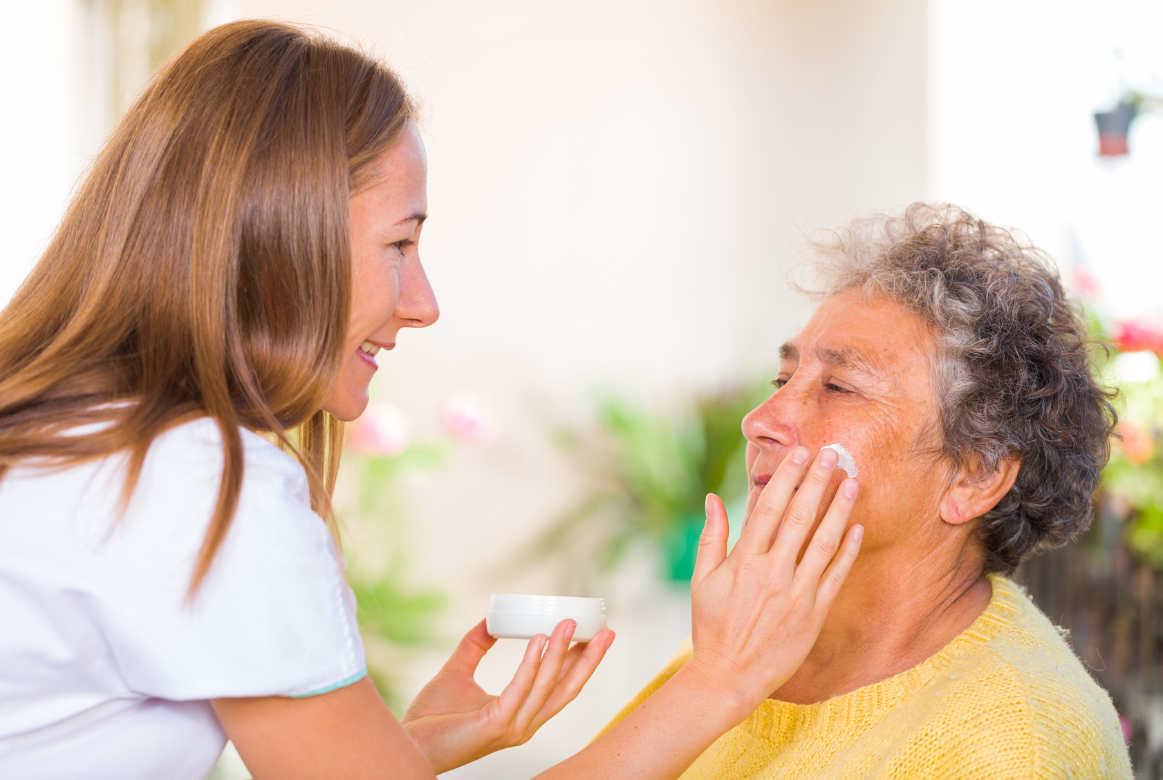 Caregiver rubs the face cream on the elderly womans face